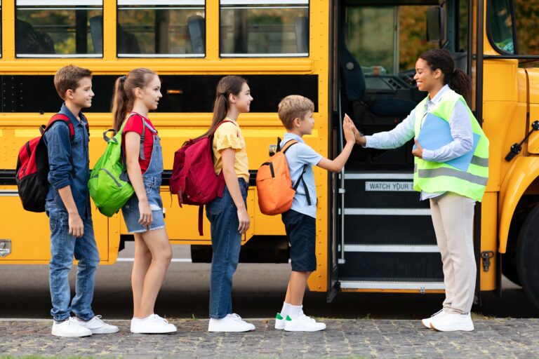 School children boarding yellow bus with safety supervisor